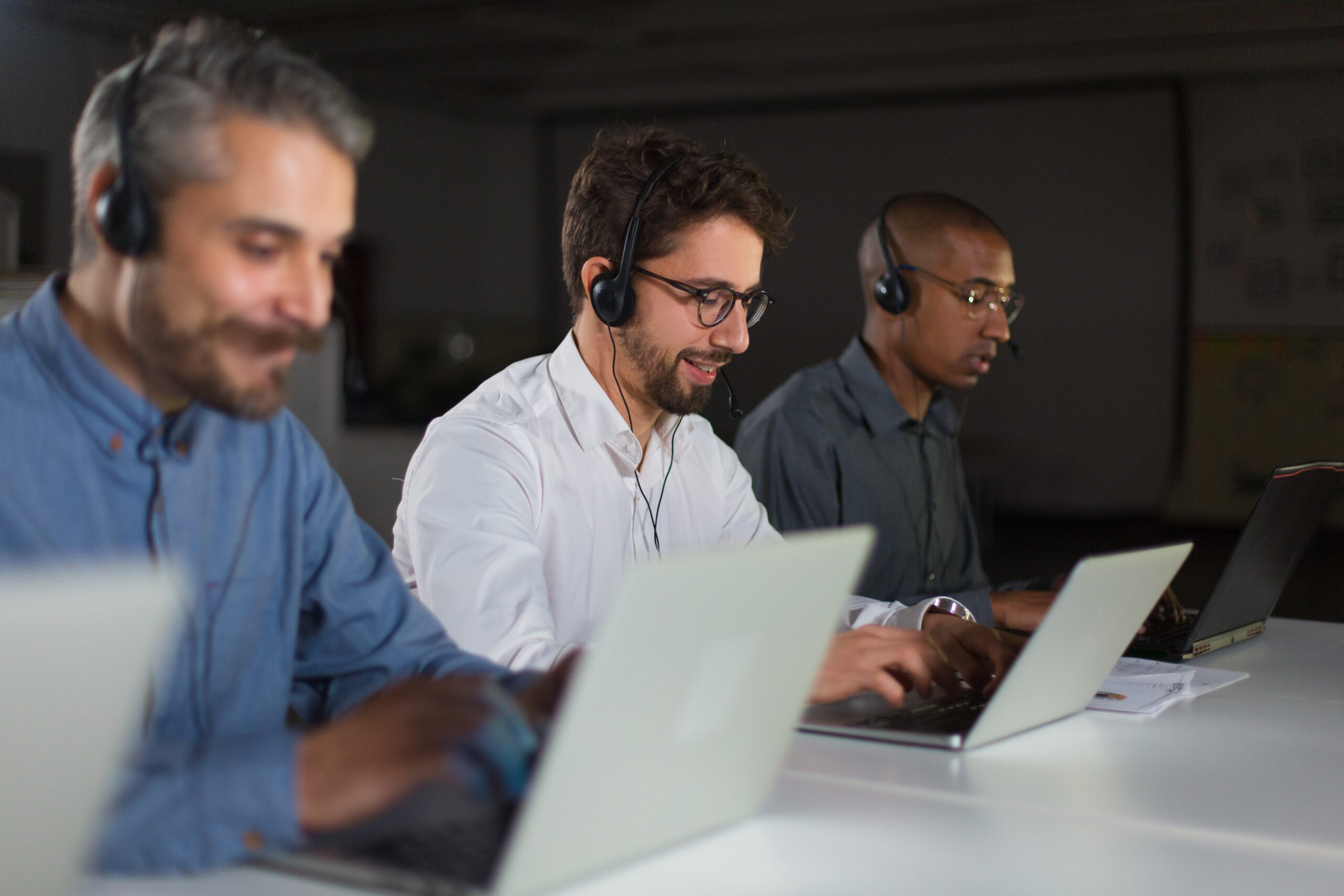 Three customer support agents wearing headsets working on laptops