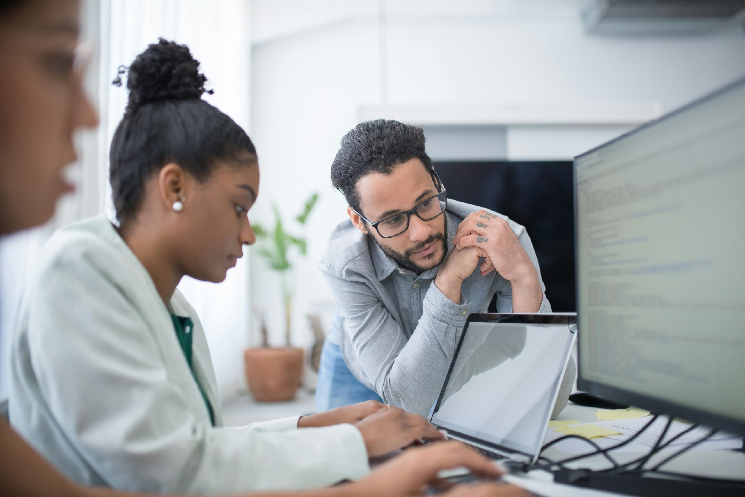 Girl typing on a laptop with a monitor with two people watching